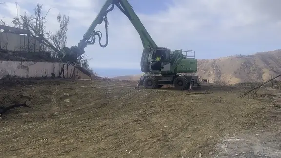 Green tree handler clearing a hillside overlooking the coast
